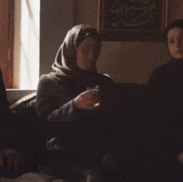 a woman wearing a hijab is sitting at a table holding a cup of coffee .