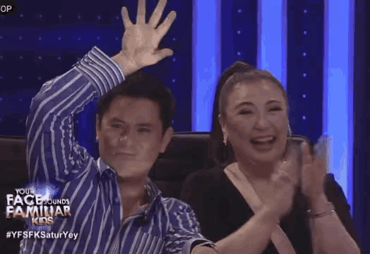 a man and a woman are sitting in a chair with their hands in the air and clapping .