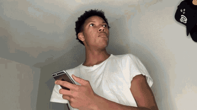 a young man in a white shirt holds a cell phone in his hand