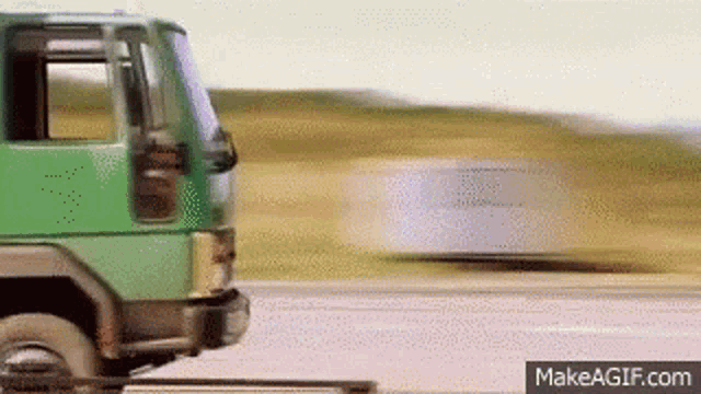 a green truck is driving down a road next to a white trailer