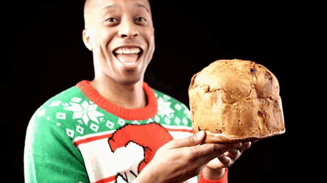 a man wearing an ugly christmas sweater is holding a large loaf of bread