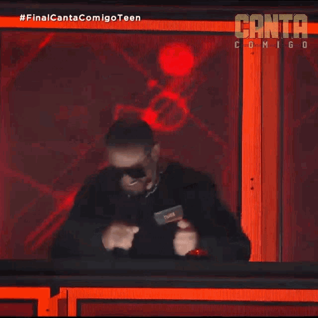 a man wearing sunglasses is standing in front of a sign that says canta comigo teen