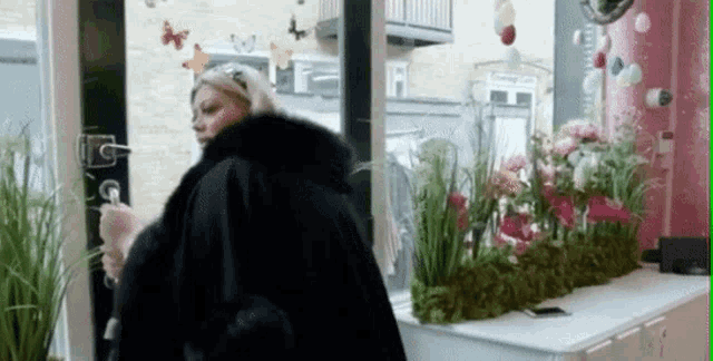 a woman in a fur coat is standing in front of a window with butterflies on it .
