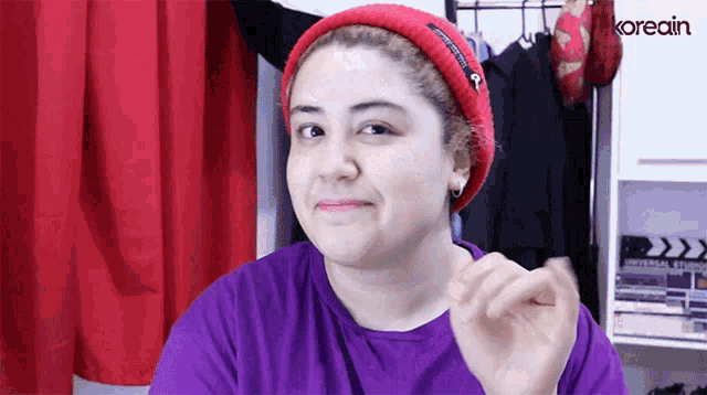 a woman wearing a red beanie and a purple shirt with the word koreain behind her
