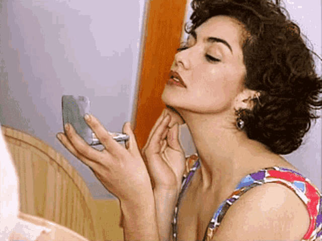 a woman is applying makeup to her face and looking at herself in the mirror
