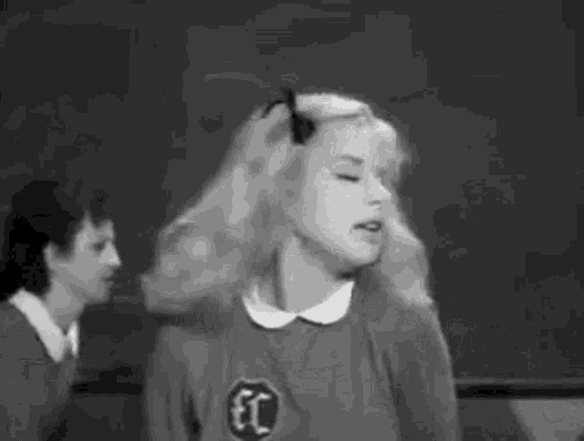 a black and white photo of a girl dancing in front of a blackboard .