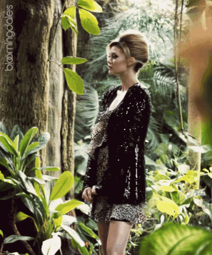 a woman in a black sequined jacket stands in a jungle with the words bloomingdale 's on the bottom