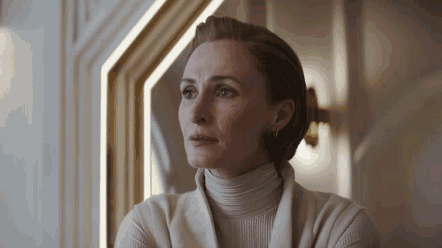 a woman wearing a white turtleneck sweater is looking out a window