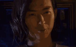 a close up of a man 's face with long hair and a dark background .