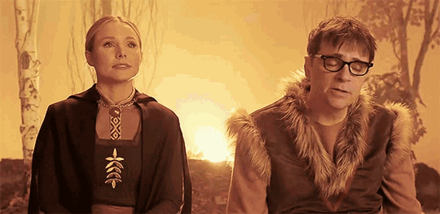 a man and a woman sitting next to each other with a fire in the background