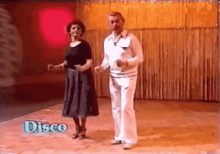 a man and a woman are dancing on a dance floor with a disco sign in the background .