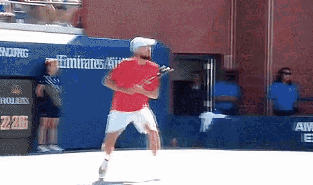 a man in a red shirt is playing tennis in front of a wall that says emirates