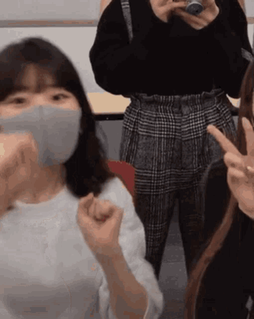 a woman wearing a mask is giving a peace sign while standing next to another woman .