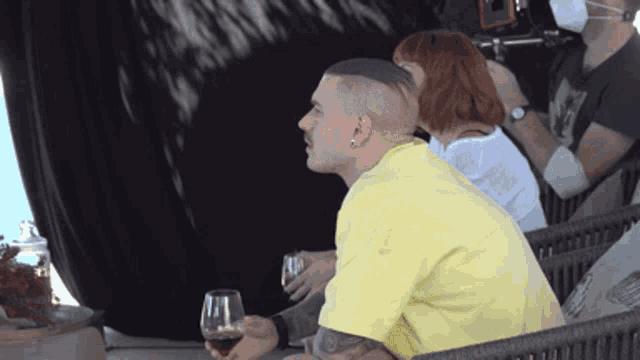a man in a yellow shirt is holding a glass of red wine