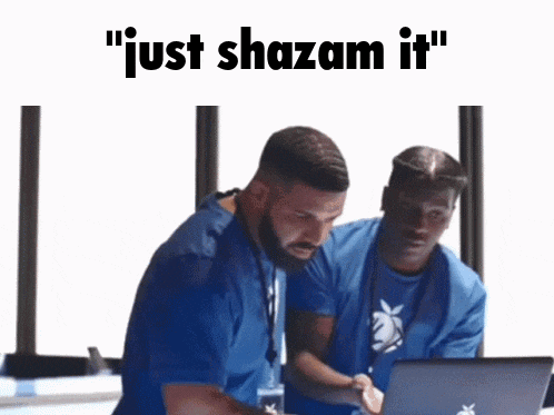 two men are sitting in front of a laptop with the words " just shazam it " above them .