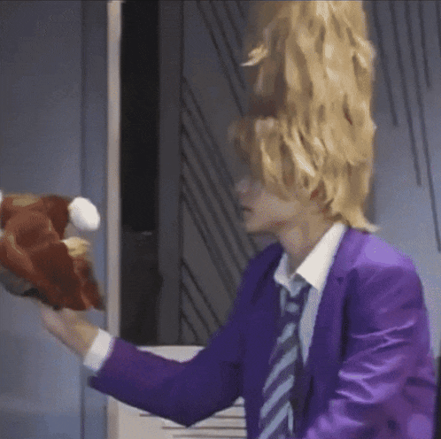 a man in a purple suit and tie is holding a stuffed animal