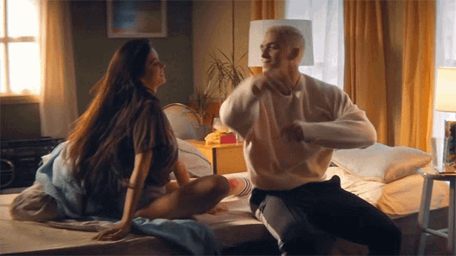 a man and a woman are sitting on a bed and dancing