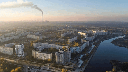 an aerial view of a city with a river and smoke coming out of the chimneys