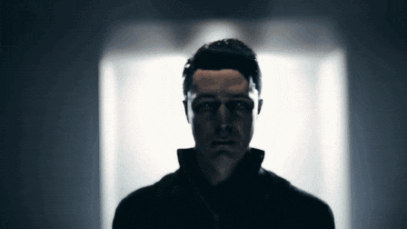 a man in a black jacket is standing in a dark room looking at the camera
