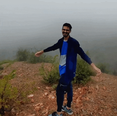 a man in a blue jacket is standing on a hill with his arms outstretched .