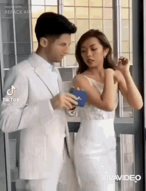 a bride and groom are standing next to each other in front of a window .