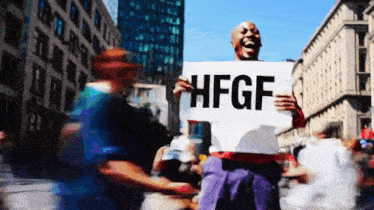 a man holding a sign that says hfgf in front of a crowd