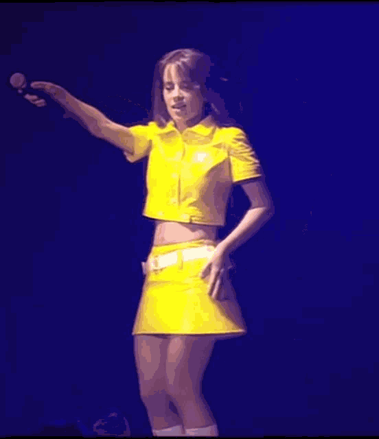 a woman in a yellow dress is singing into a microphone on stage .