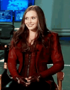 a woman in a red jacket is sitting in a chair smiling .