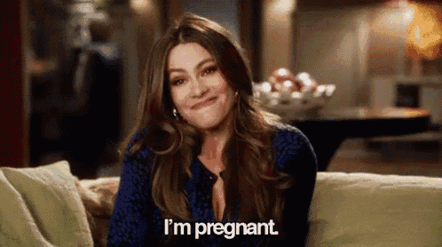 a woman is sitting on a couch and smiling while talking about being pregnant .