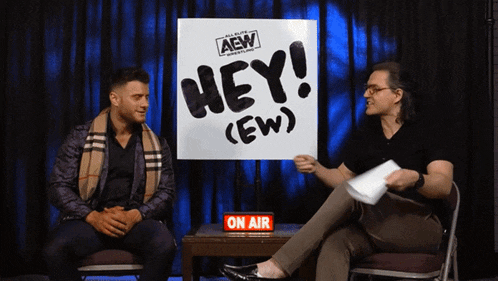 two men sitting in front of a sign that says hey