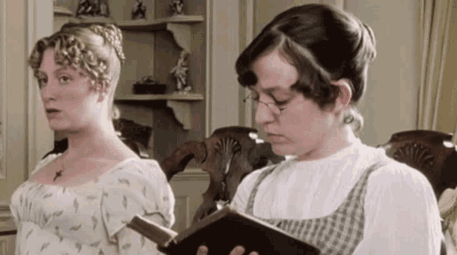 two women are standing next to each other one reading a book