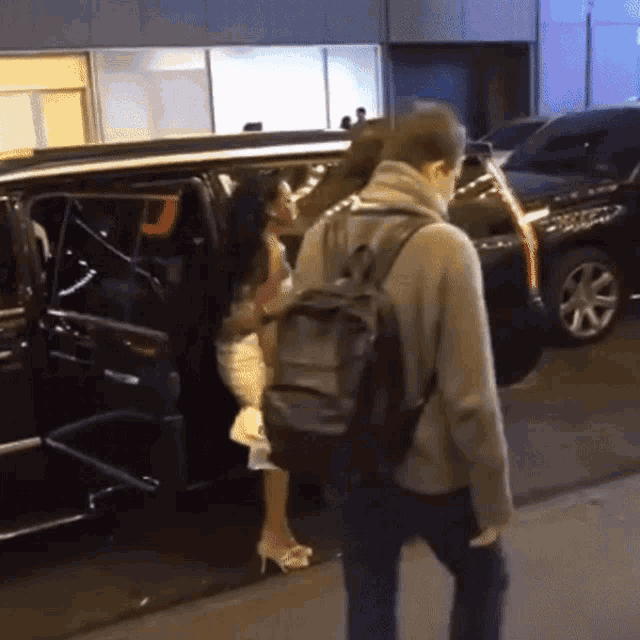a man with a backpack is standing next to a woman getting out of a limousine