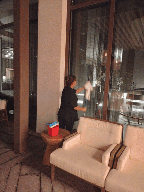 a woman cleaning a window with a mop in front of a couch