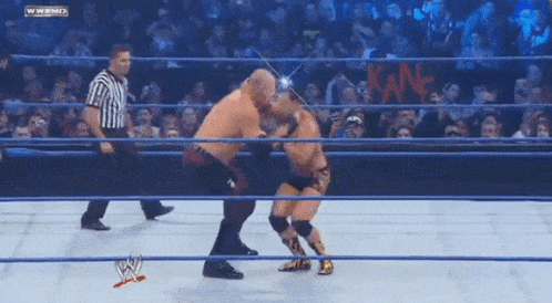 two men are wrestling in a wrestling ring with a referee and a crowd watching ..