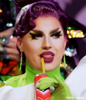 a drag queen with purple hair and green gloves is drinking from a can with a straw .