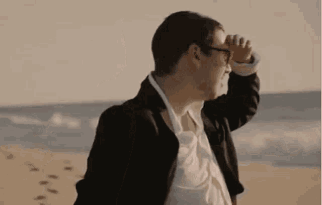 a man in a suit and glasses is standing on the beach .