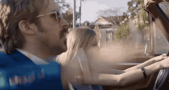 a man with a mustache is driving a car with a woman sitting in the back seat .