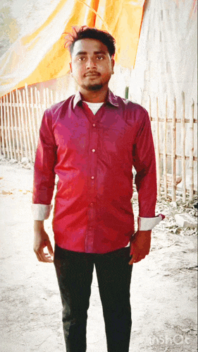 a man in a red shirt and black pants stands in front of an orange tarp