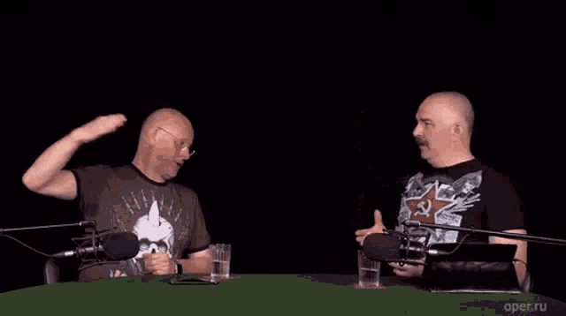 two men are sitting at a table in front of microphones .