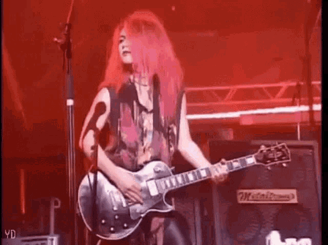 a woman with pink hair is playing a guitar on a stage in front of a microphone .