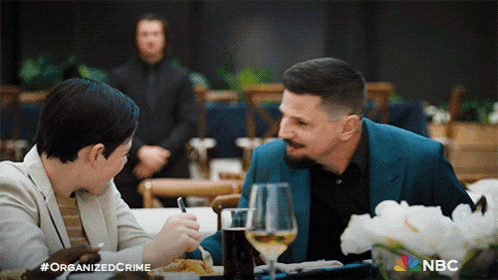 a man and a woman are sitting at a table with a nbc logo in the background
