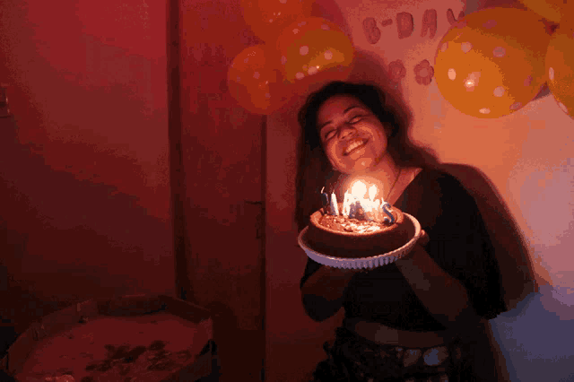 a woman blows out candles on a cake in front of balloons that say b-day