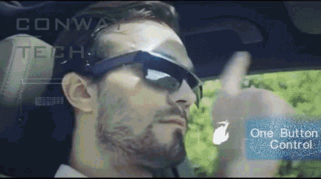 a man wearing sunglasses is driving a car with a one button control displayed on the screen