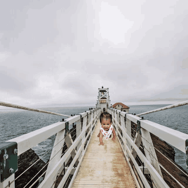 a baby is crawling across a wooden bridge over the ocean