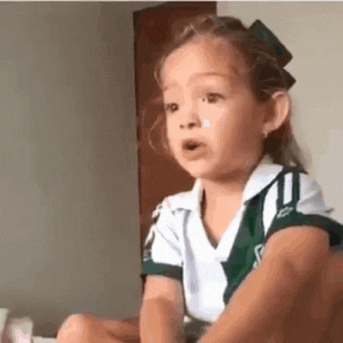 a little girl wearing a green and white shirt is sitting on a bed .