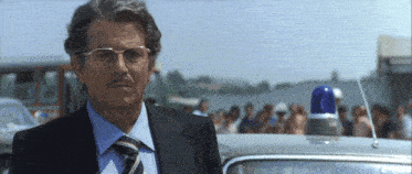 a man in a suit and tie stands in front of a car