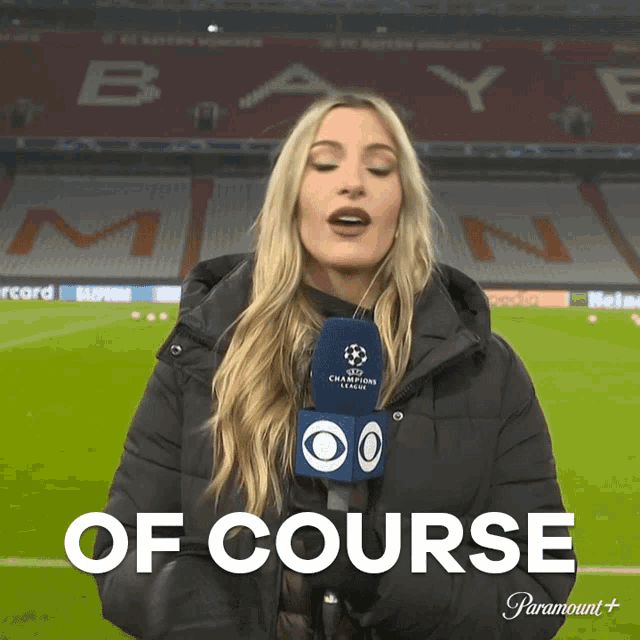 a woman holding a microphone on a soccer field that says " of course "
