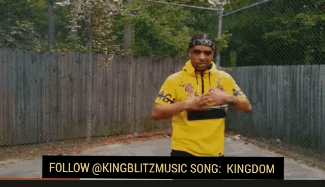 a man in a yellow shirt is standing in front of a chain link fence with the words follow @kingblitzmusic song kingdom below him