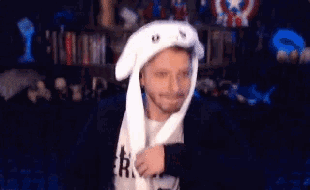 a man wearing a white bunny hat with moving ears is standing in front of a bookshelf .