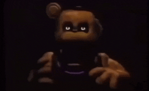 a teddy bear with glowing eyes is holding a remote control in his hands in a dark room .